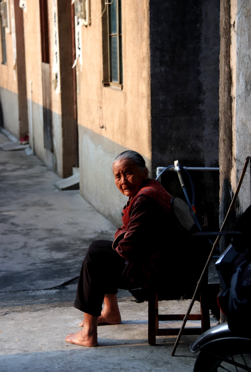 村中一个阿婆打着赤脚,正坐在墙根晒太阳.