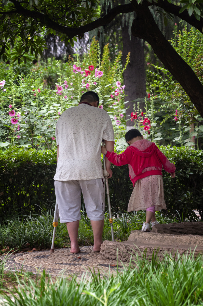 在人民公园内一个很懂事的小女孩搀扶着她的爸爸她爸爸的腿受伤了正光